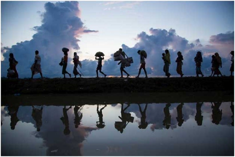 Un grupo de migrantes y refugiados caminan en fila, cargando algunas pertenencias Foto: Acnur