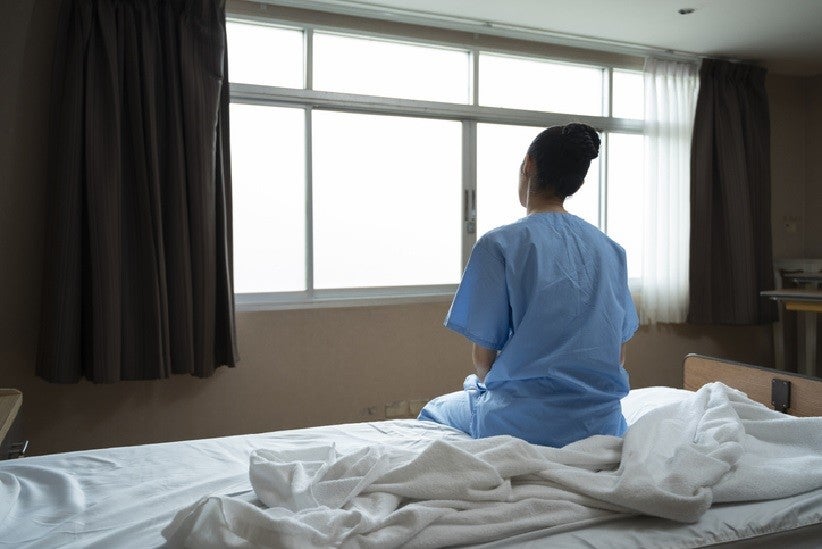 Mulher sentada em cama de hospital olhando pela janela