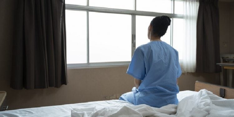 Mulher sentada em cama de hospital olhando pela janela