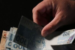 Registro de uma mão segurando algumas cédulas de reais com notas de 100 e 50. Foto: José Cruz/Agência Brasil