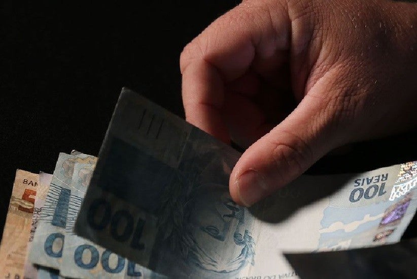 Registro de uma mão segurando algumas cédulas de reais com notas de 100 e 50. Foto: José Cruz/Agência Brasil
