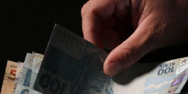 Registro de uma mão segurando algumas cédulas de reais com notas de 100 e 50. Foto: José Cruz/Agência Brasil